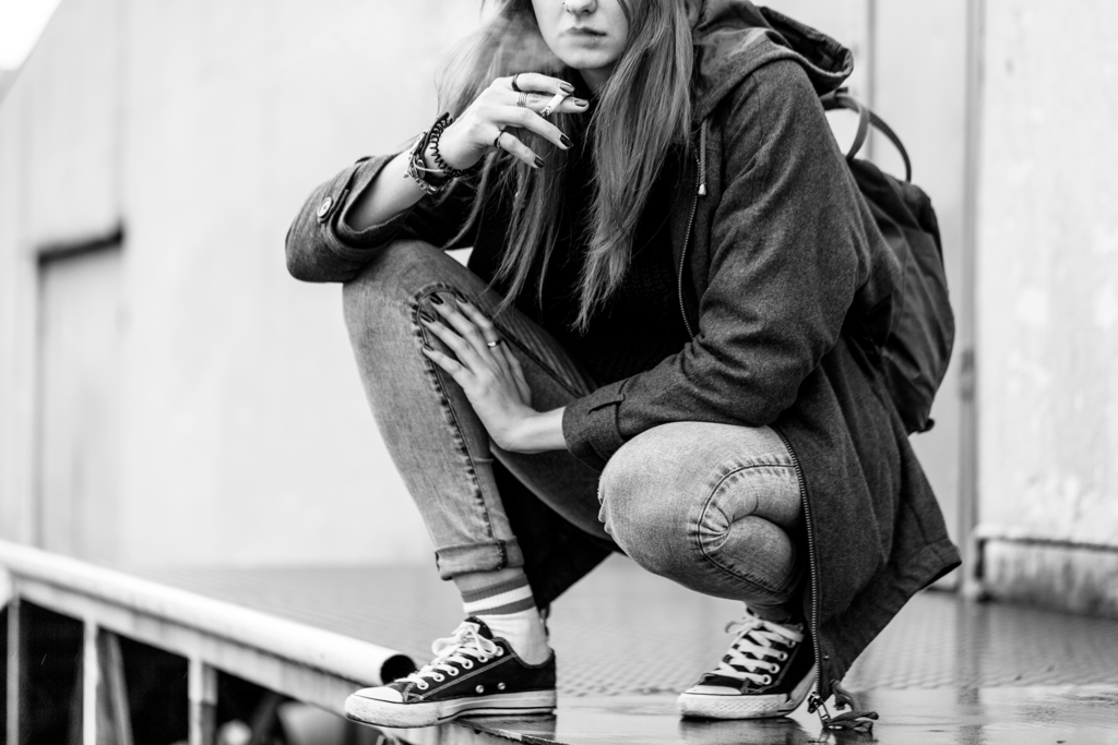 Black and white photo of a girl crouching down smoking a cigarette