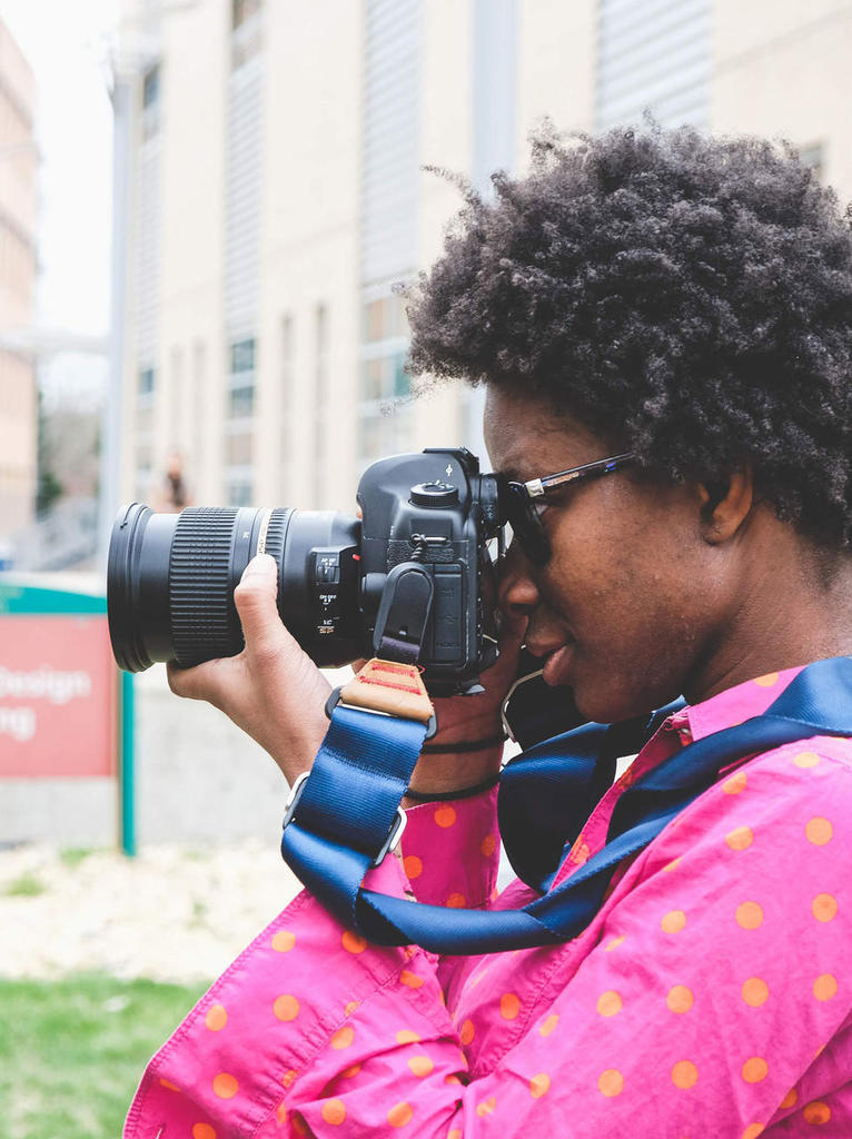 Mason art student holding camera up to her face and looking through viewfinder outside
