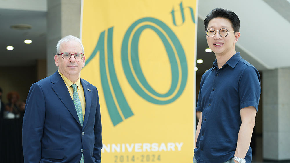 Two men, one in blue blazer, the other in short-sleeve blue shirt. Both wearing glasses.