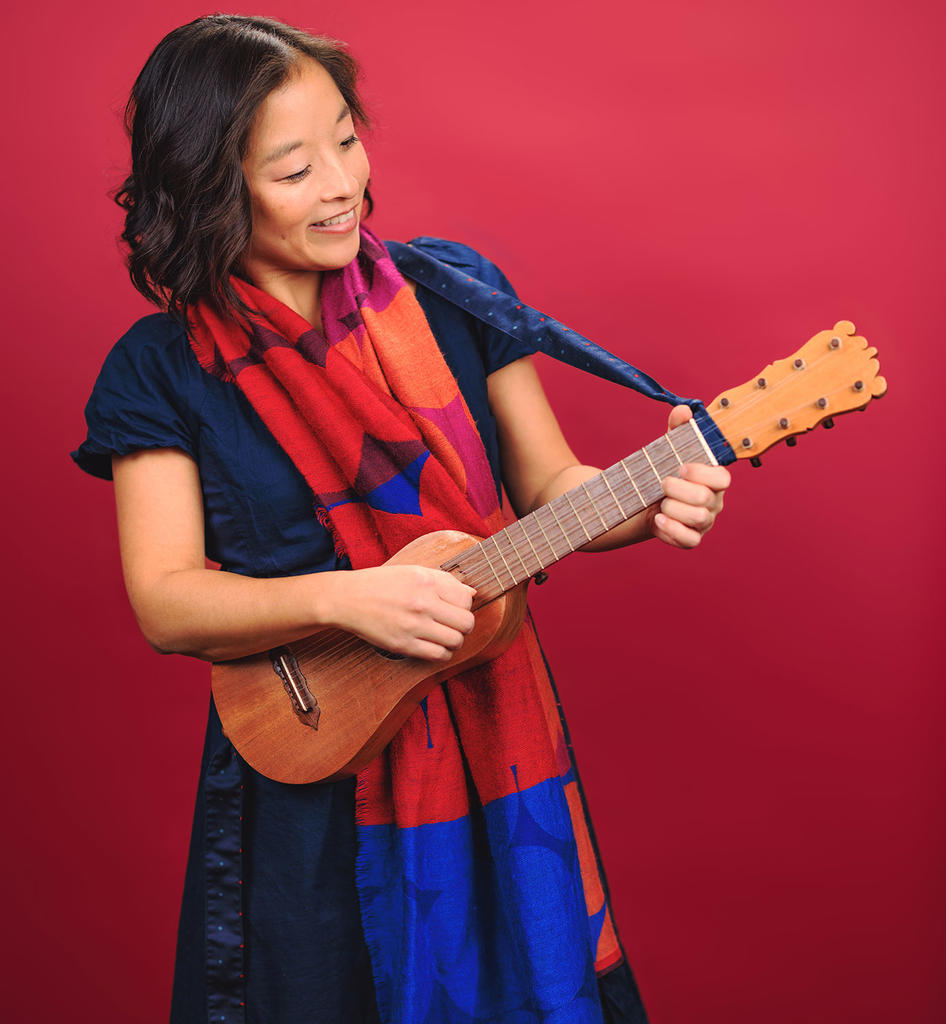 Asian woman dressed in blue playing a guitar against a red background