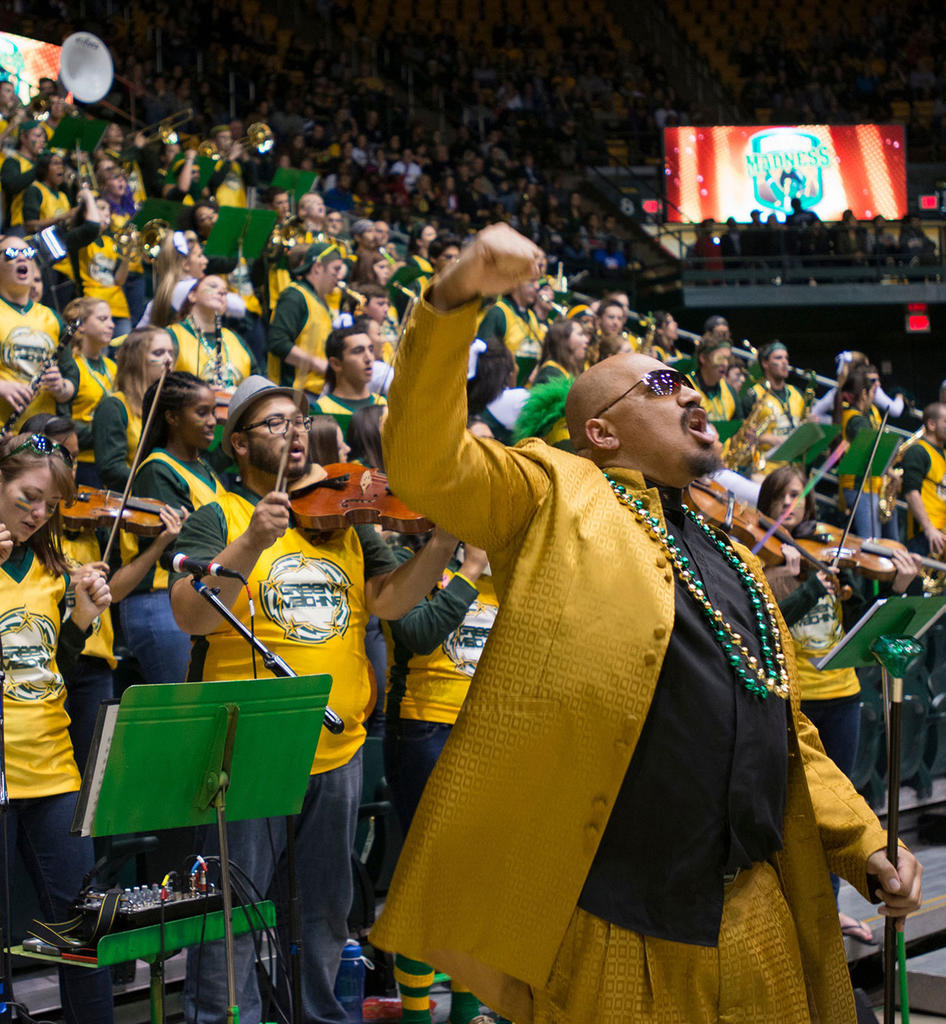 Doc Nix dressed in yellow and with fist raised in air in front of his Green Machine at Eagle Bank stadium