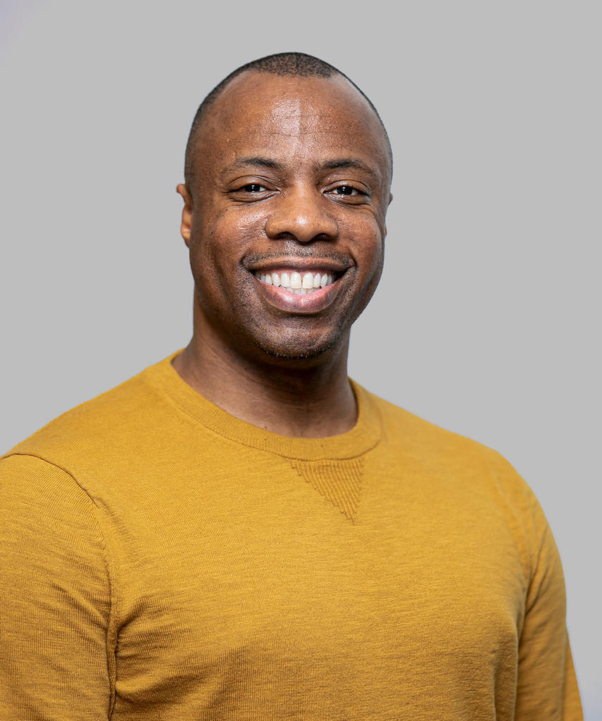 Black man wearing yellow round-necked sweater smiling at the camera