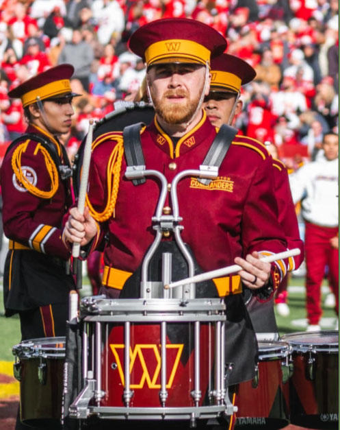 Paul Bernfield dressed in Washington Commanders uniform carrying a drum set and marching