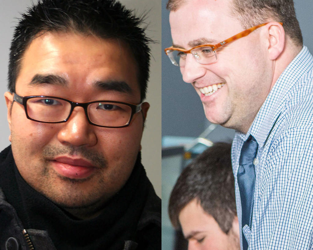 Asian man with dark hair, dark glasses, wearing black looking at camera and a white male wearing a checkered shirt and blue tie seen from the side smiling