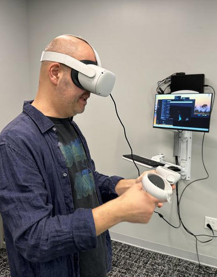man wearing a virtual reality headset, holding a set of controls with a TV screen in background