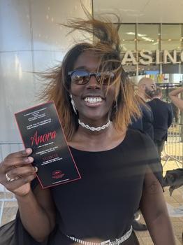 Rhyan Ellliott, a young, African-American woman holding up a playbill for the movie Anora standing outside a theater