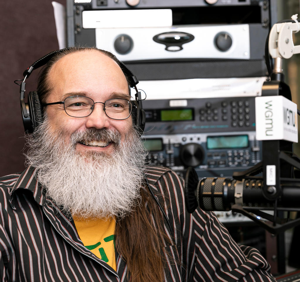 James Casey, director of the VSGI, smiling with big white beard, striped shirt, glasses and wearing headphones