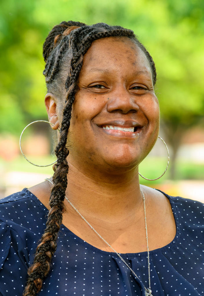 African American woman with braid down one side of head wearing navy and white polka dot dress and large hoop earrings