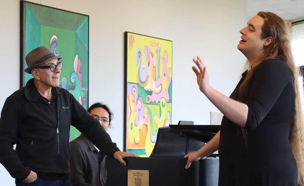Ricky Ian Gordon working with a George Mason opera student in the Center for the Arts mezzanine with a young man accompanying them on grand piano behind them