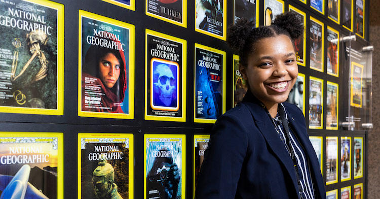 Sonja Phillips-Thomas standing in front of a wall of National Geographic Magazines at the National Geographic location where she interned