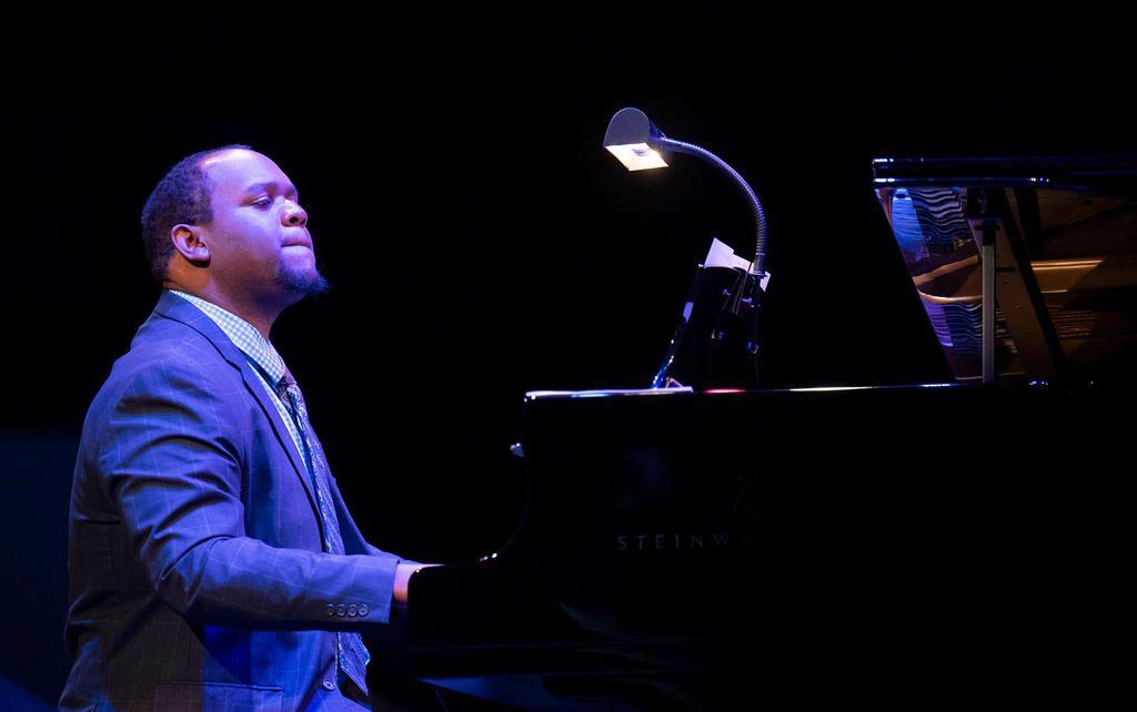 Paul Bratcher: an African American man wearing a pinstripe suit and sitting at a grand piano