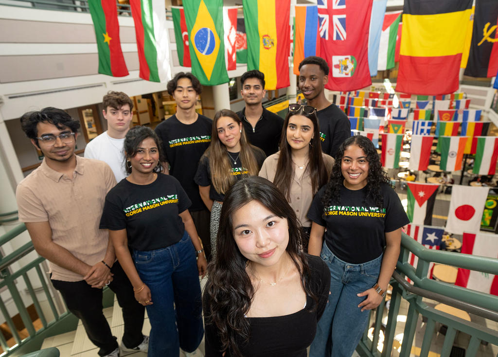 group of international students standing in front of many colorful flags inside a building