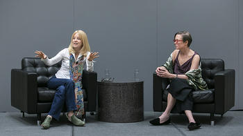 At left, composer Maria Schneider in white shirt, colorful silk scarf, and jeans, speaks to the audience, sitting next to moderator Sandra Aistars, George Mason University Antonin Scalia Law School Professor and Arts & Entertainment Advocacy Clinic Director. 